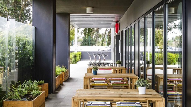 An outdoor seating area with wooden tables and benches, potted plants, and a view of the street. - ibis Lisboa Sintra (Sintra)
