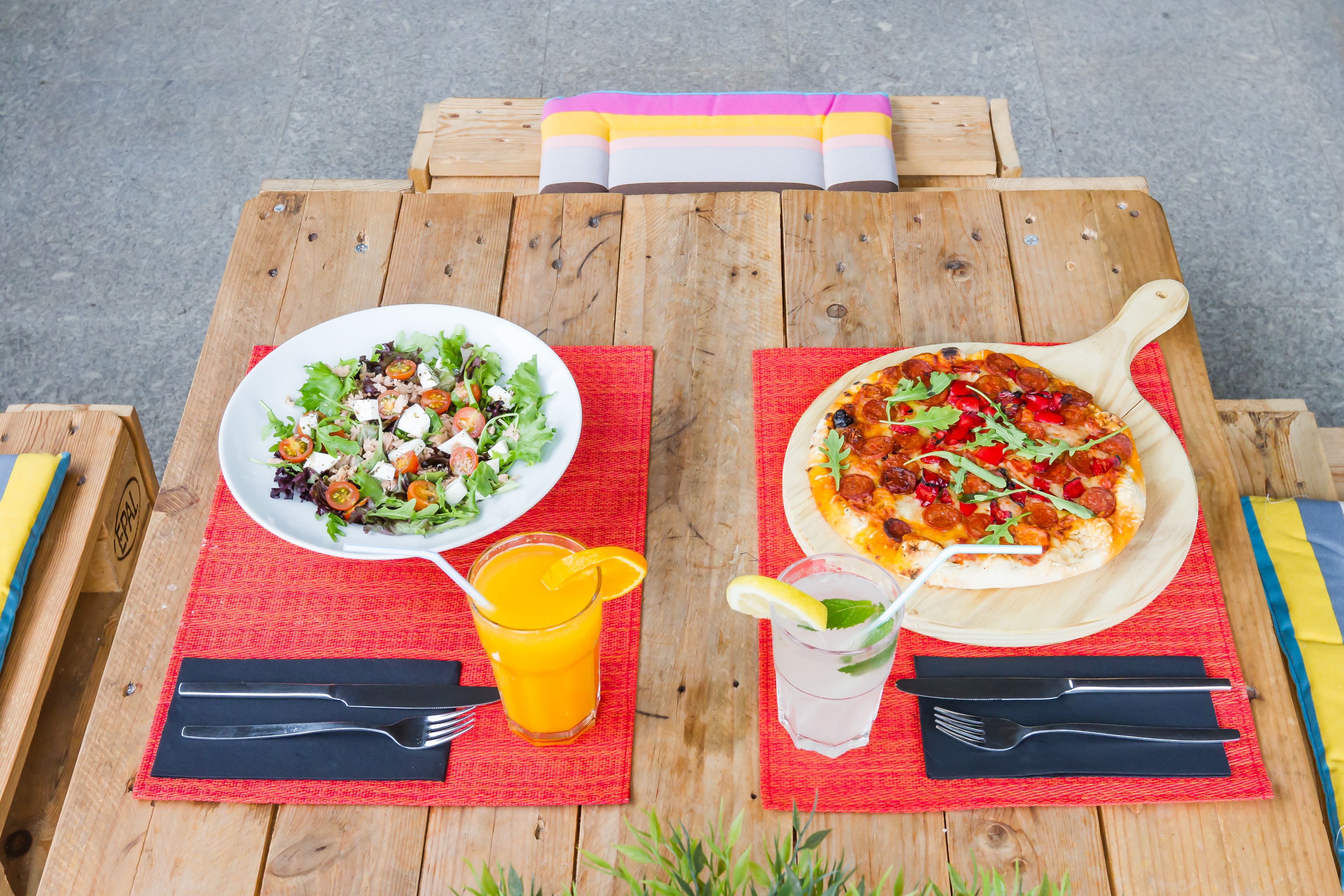Ein Holztisch mit Salat, Orangensaft, Eistee und einer Pizza.
