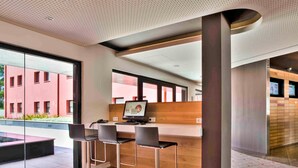 A modern workspace with a computer, three chairs, and a large window overlooking a building. - ibis Lisboa Sintra (Sintra)
