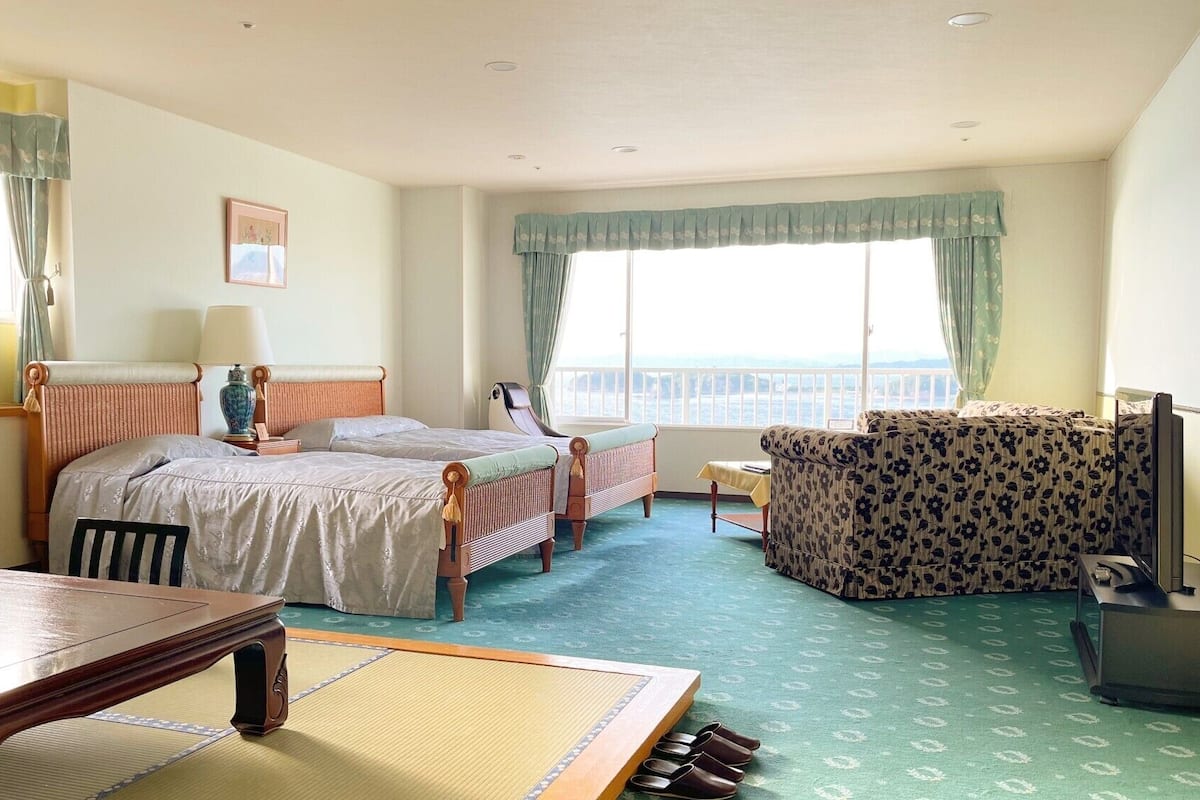 A hotel room with two beds, a sofa, a dining table, and a view of the sea.