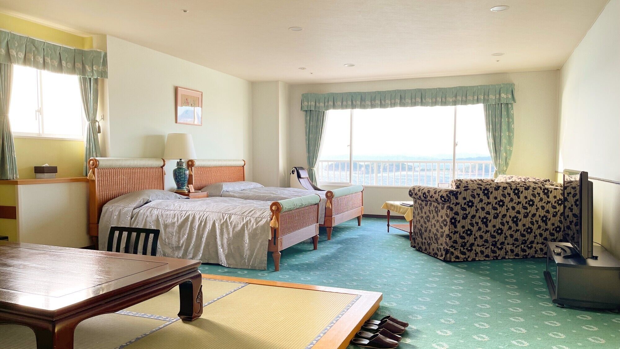 A hotel room with two beds, a sofa, a table, and a view of the sea.