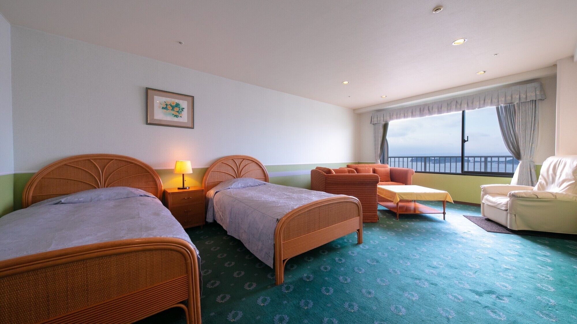 Hotellihuone, jossa on kaksi erillistä sänkyä, sohva, tuoli, pieni pöytä ja ikkuna, josta on näkymä.