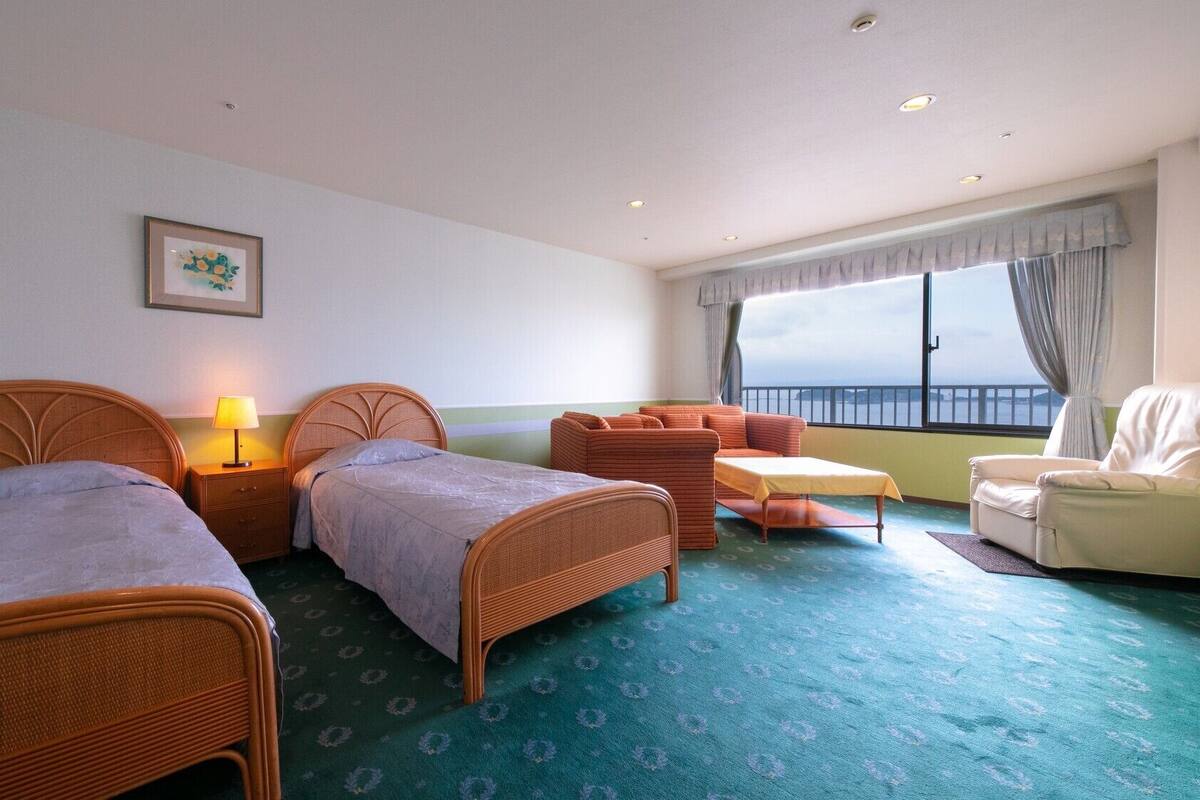 A hotel room with two single beds, a sofa, a chair, a small table, and a window with a view.