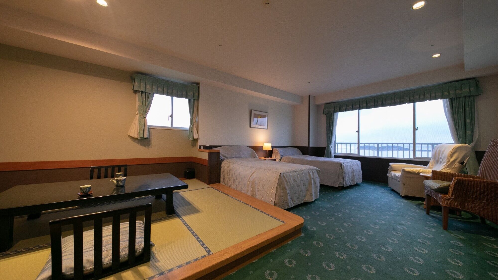 A hotel room with two beds, a dining table, a chair, and a view of the sea.