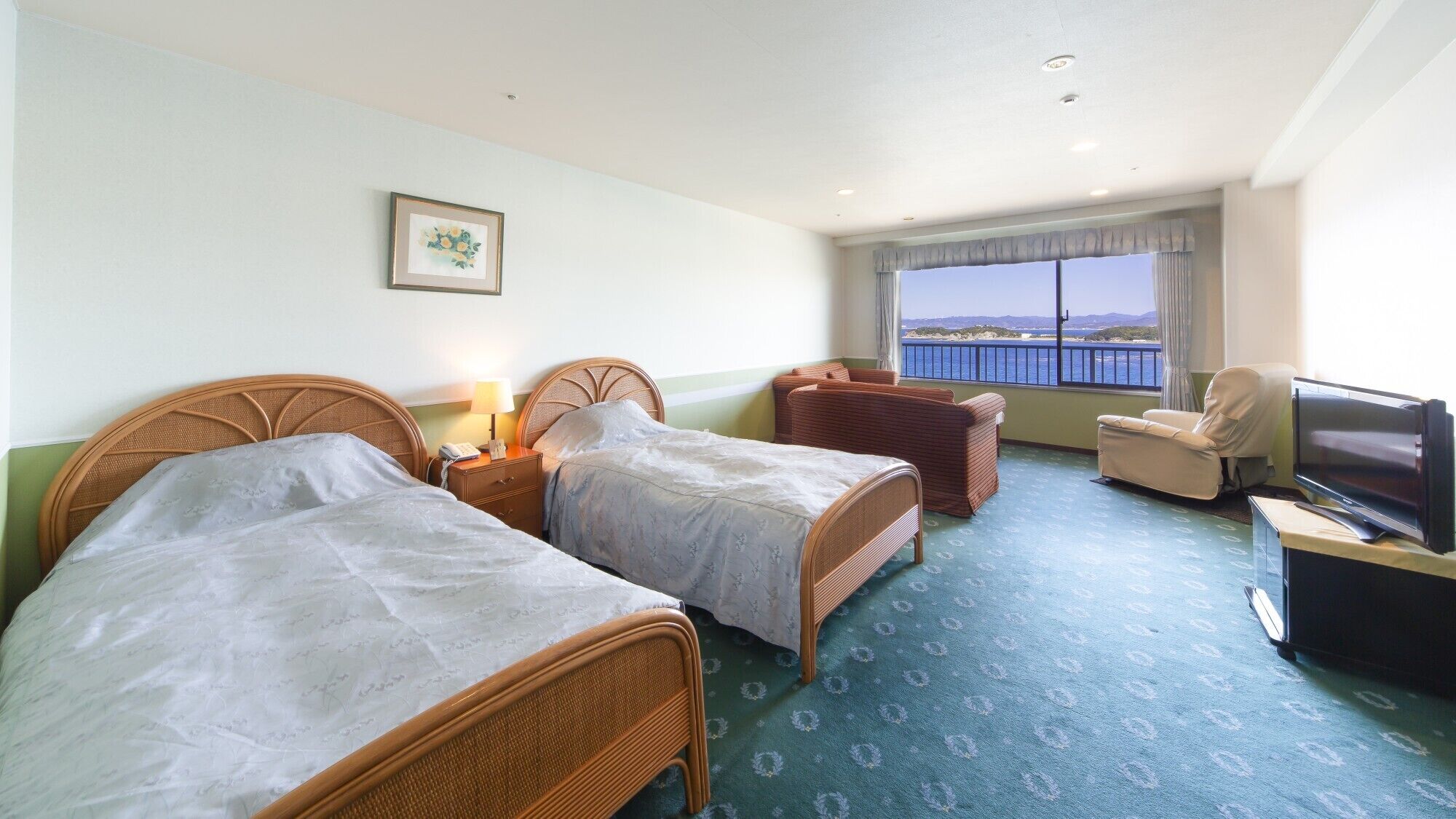 A hotel room with two beds, a television, a chair, and a view of the sea.