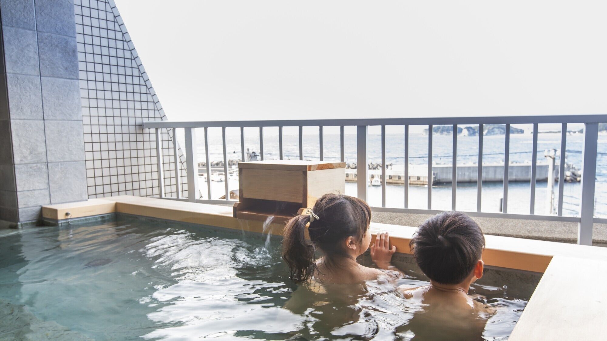 A hot tub with a view of the sea and a tiled wall.