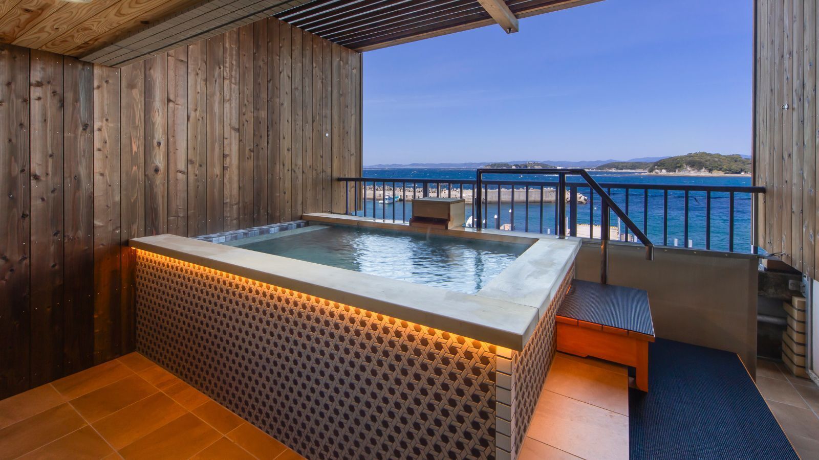 A wooden spa area with a hot tub, a bench, and a view of the sea.