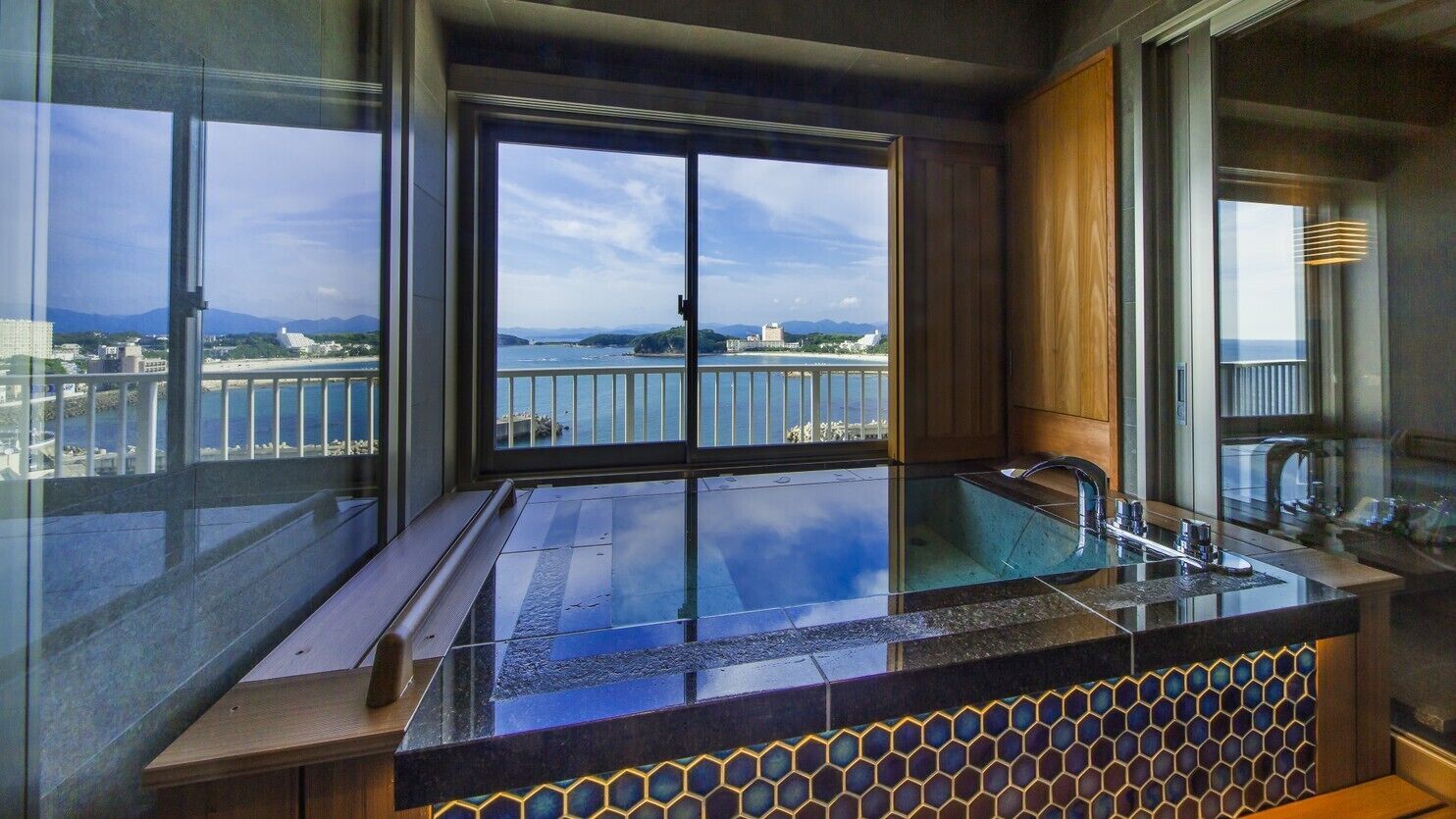 A modern bathroom with a large window, a glass-enclosed bathtub, and a view of a coastal area.