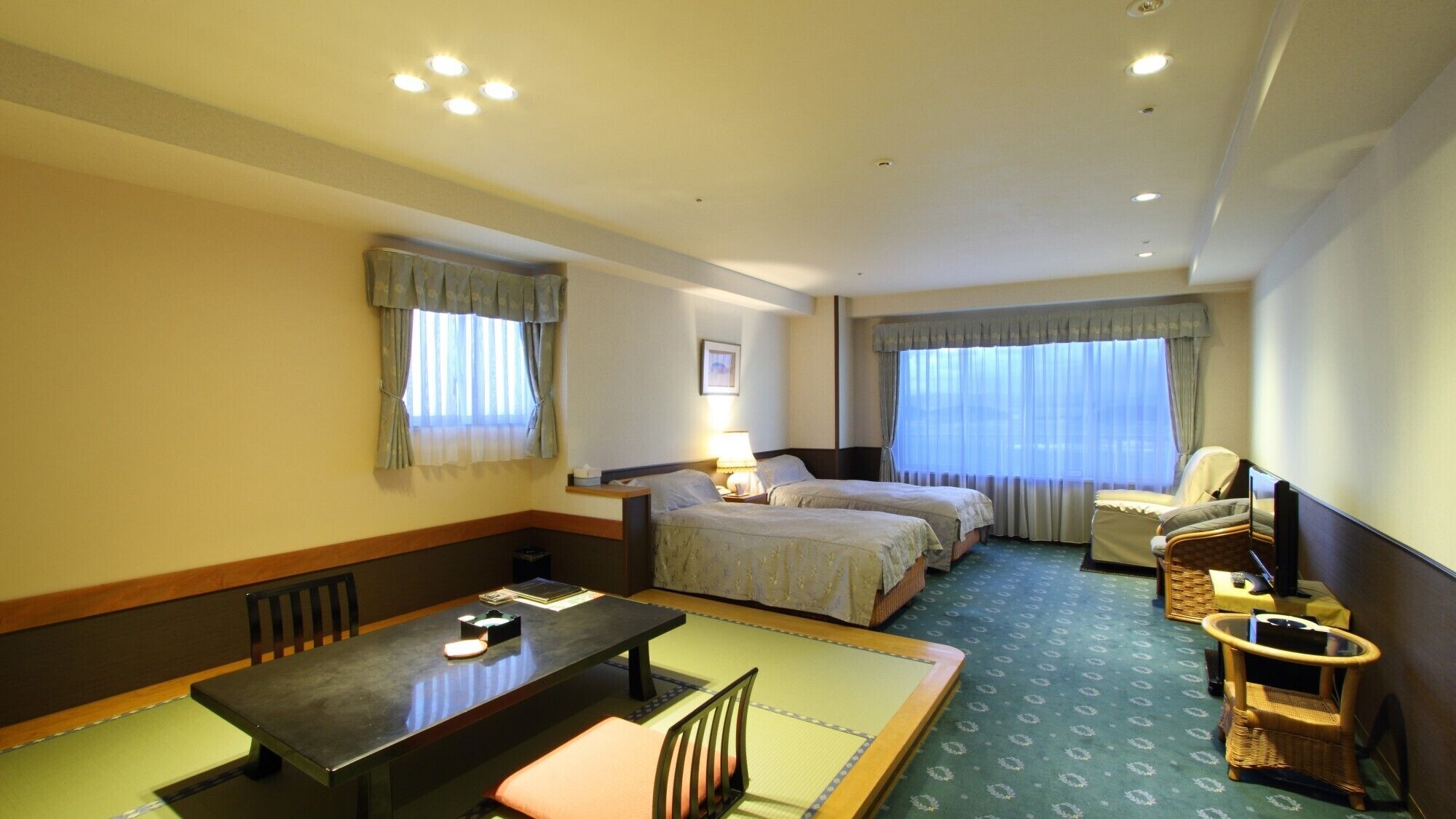 A hotel room with two beds, a desk, a chair, a television, and a window with curtains.