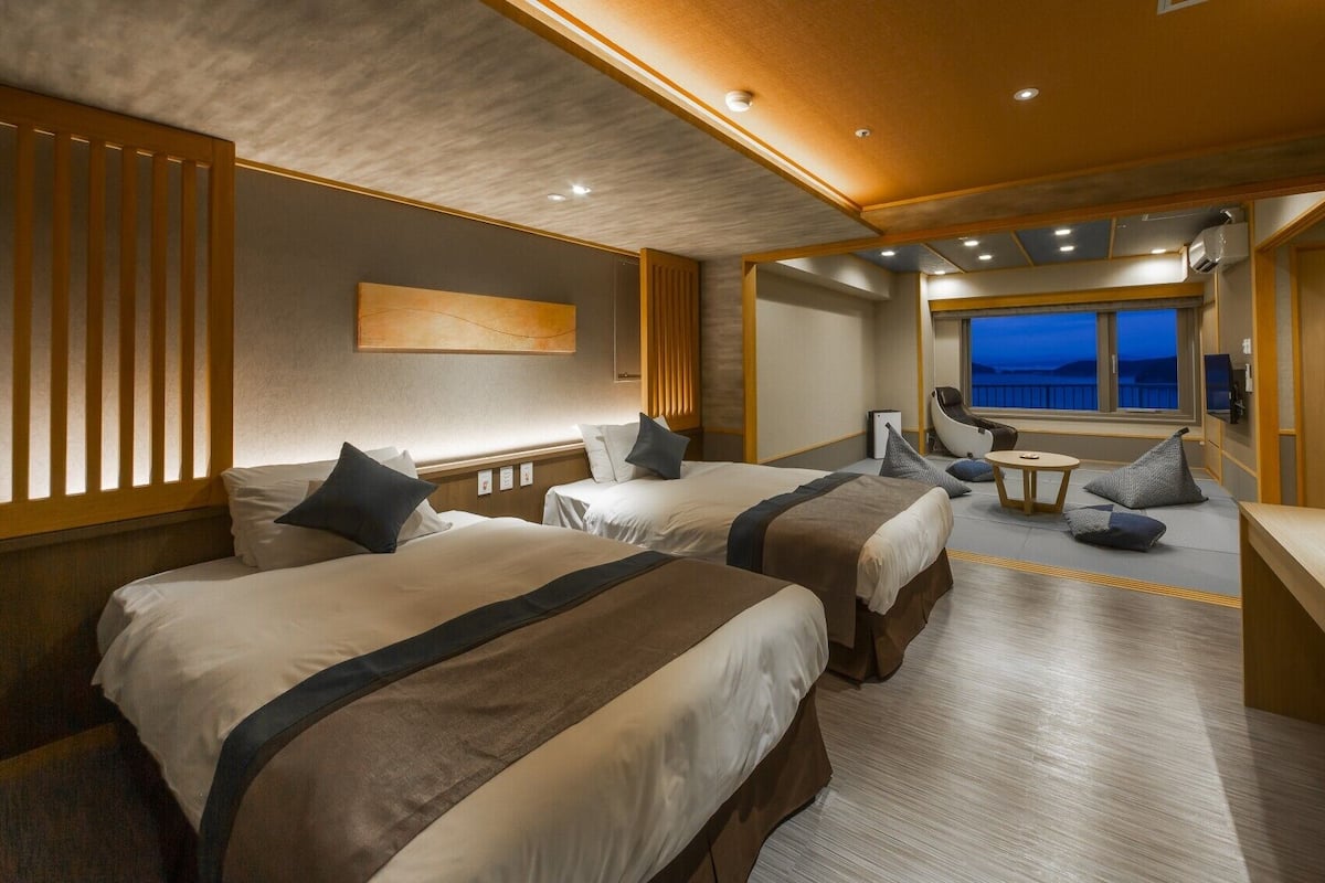 A hotel room with two beds, a seating area, and a large window with a view.
