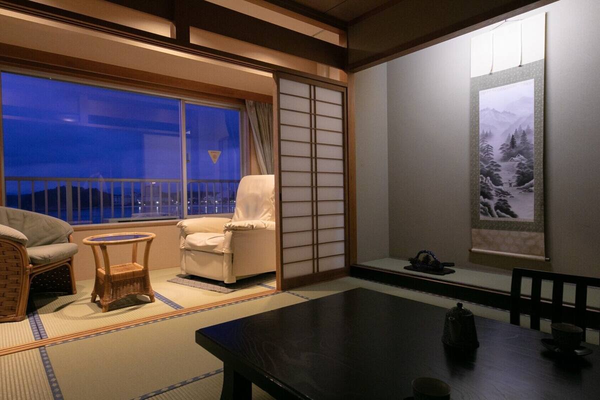 A traditional Japanese room with tatami flooring, a low table, a sofa, and a chair.