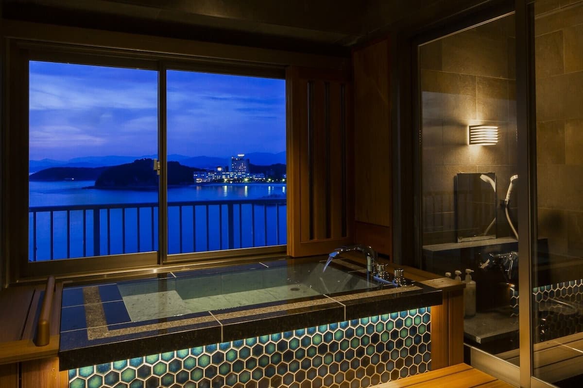 A bathtub with a view of a cityscape at dusk.