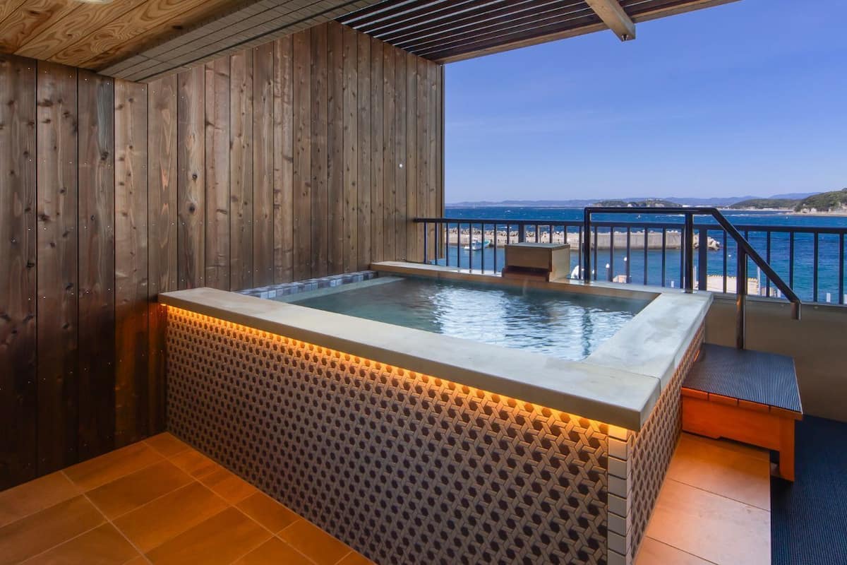 A wooden spa area with a hot tub, a bench, and a view of the sea.