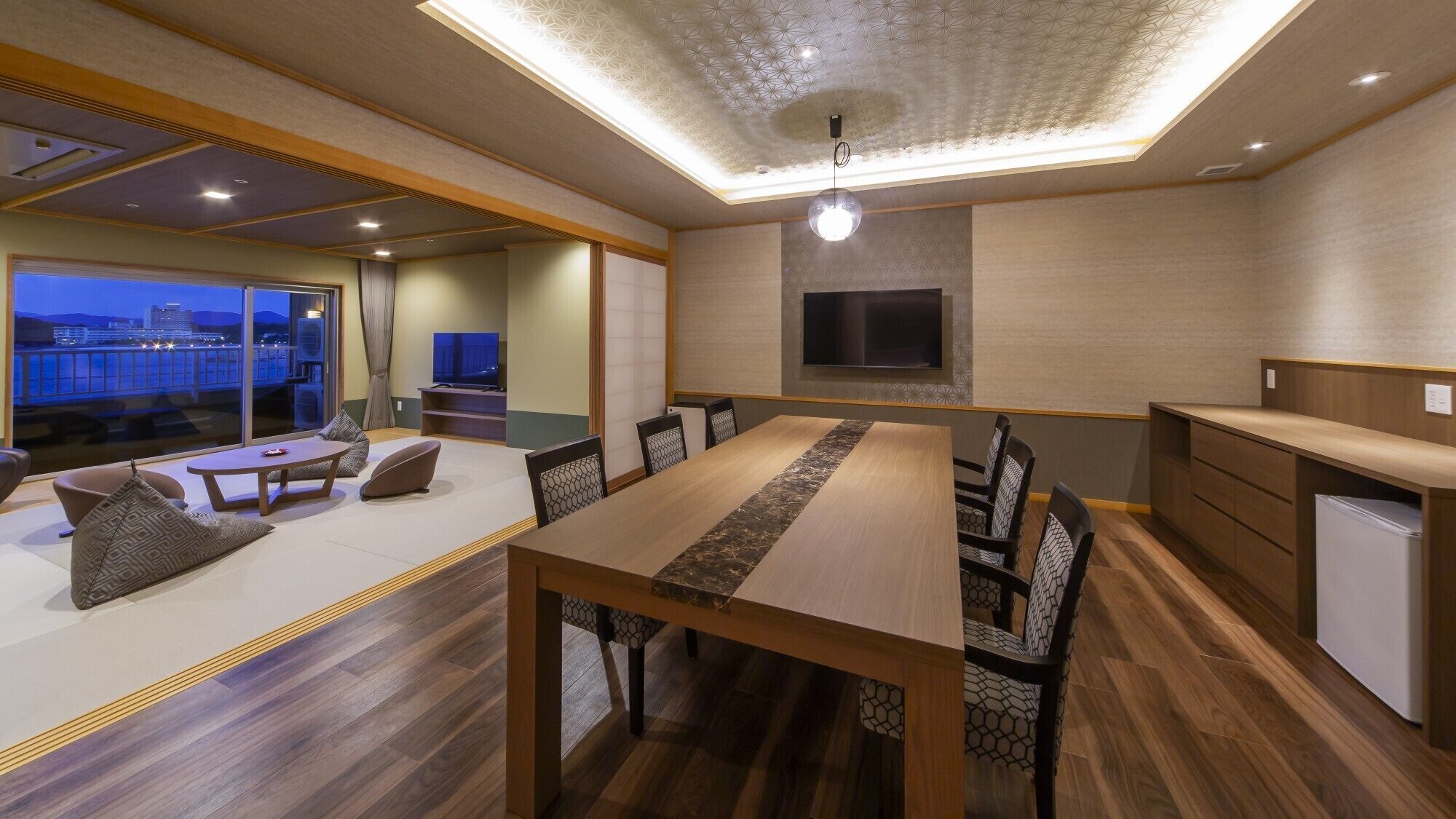 A modern interior with a dining area, seating, a flat-screen TV, and a view of the cityscape.