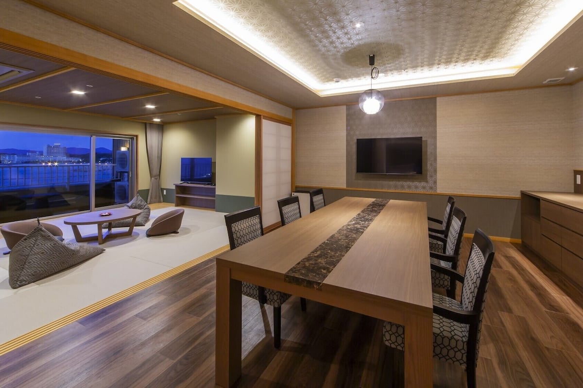 A modern interior with a dining area, seating, a flat-screen TV, and a view of the cityscape.