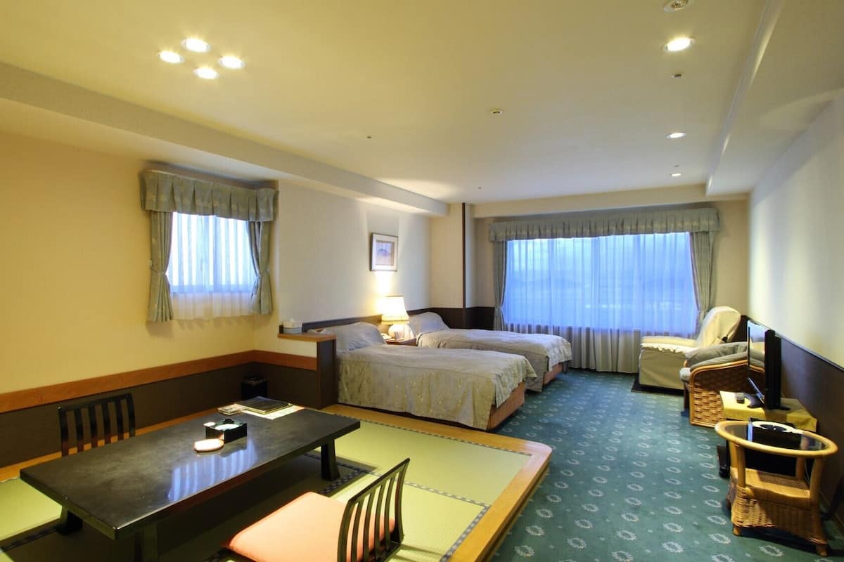 A hotel room with two beds, a desk, a chair, a TV, and a window with curtains.