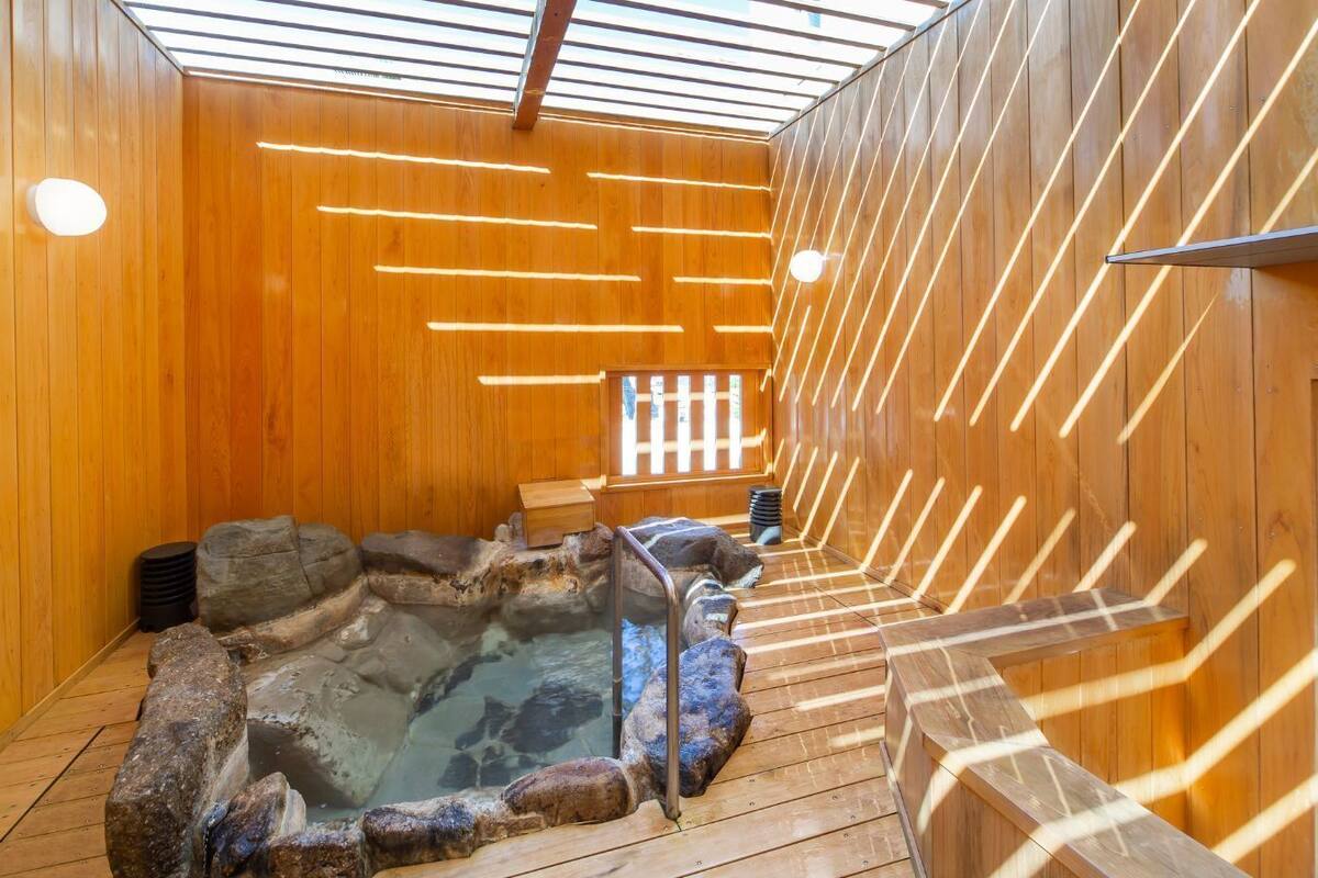 A wooden interior with a hot spring, wooden benches, and a stone wall.
