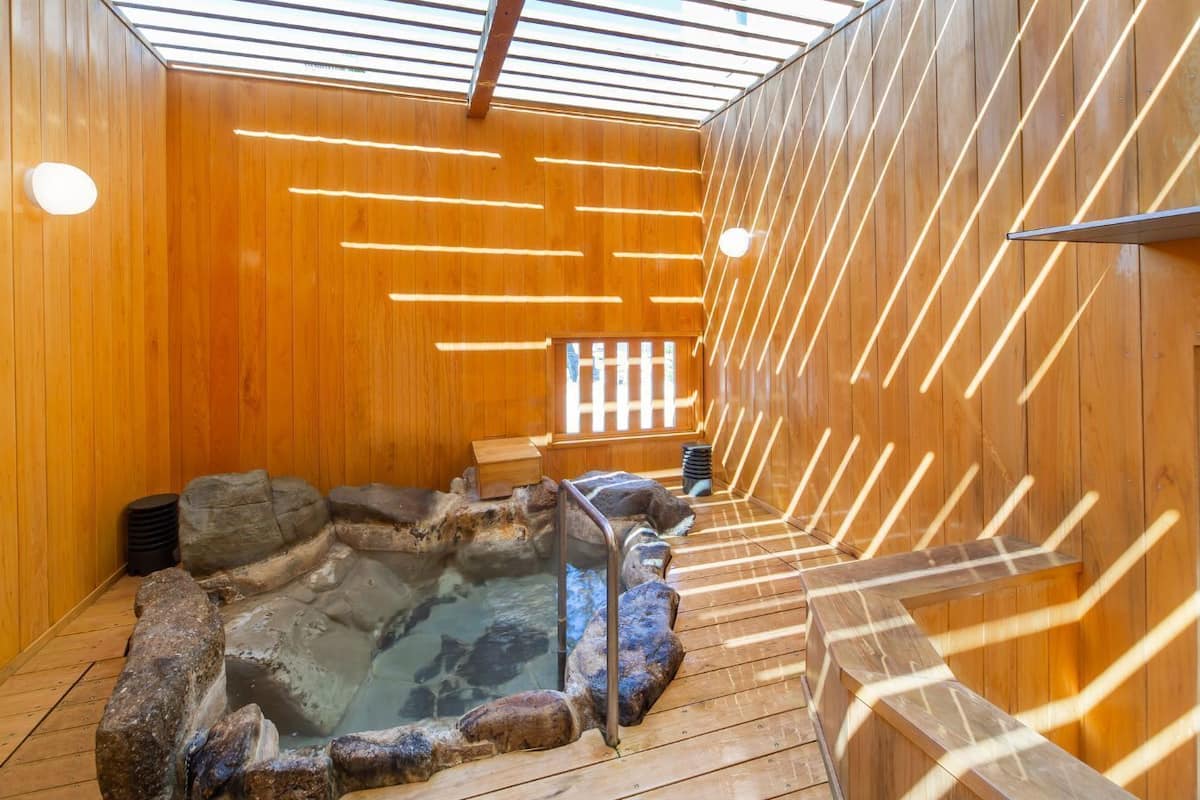 A wooden interior with a hot spring, wooden benches, and a stone wall.