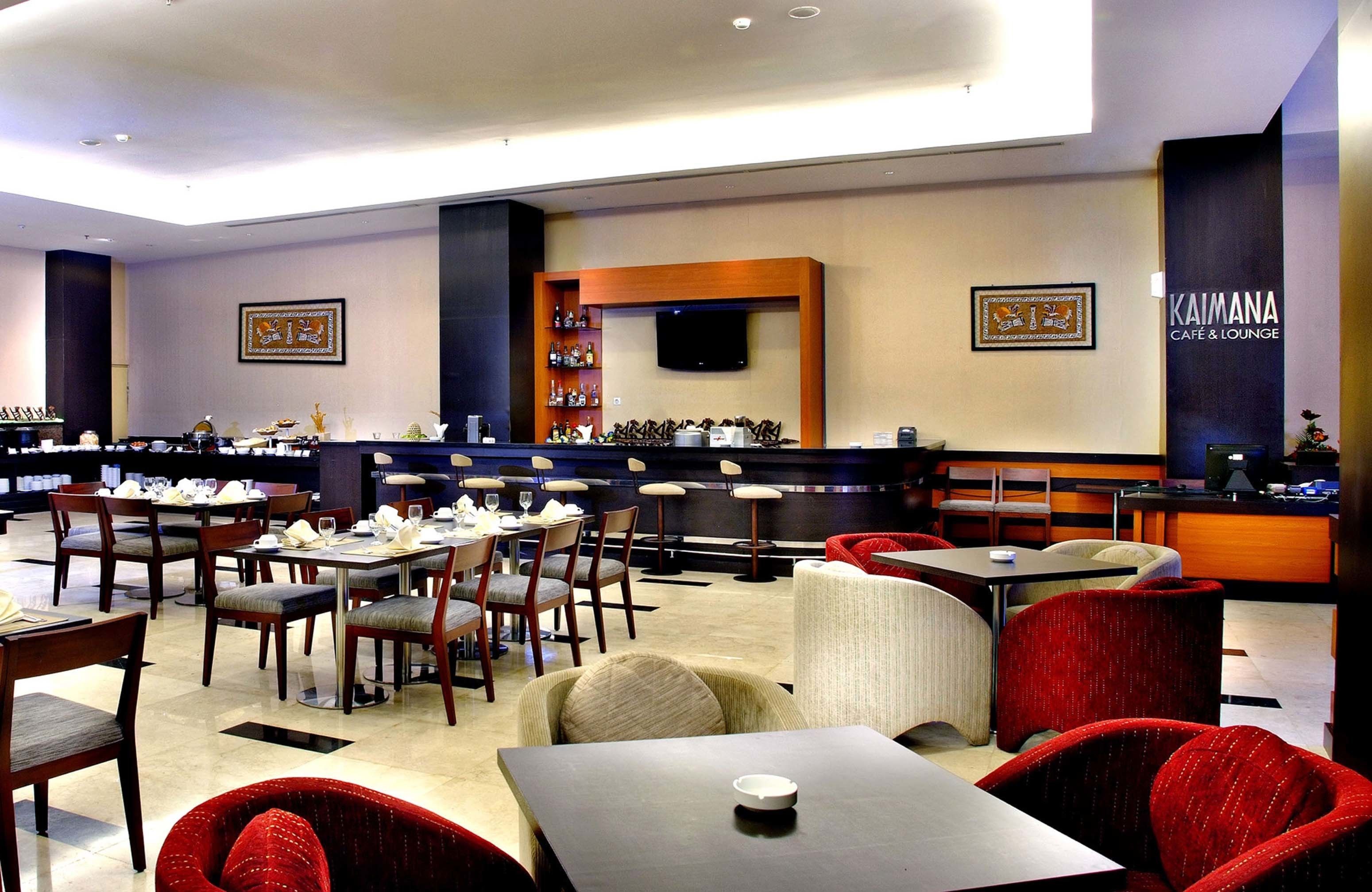 A modern cafe and lounge with multiple seating areas, a bar, and a television screen.