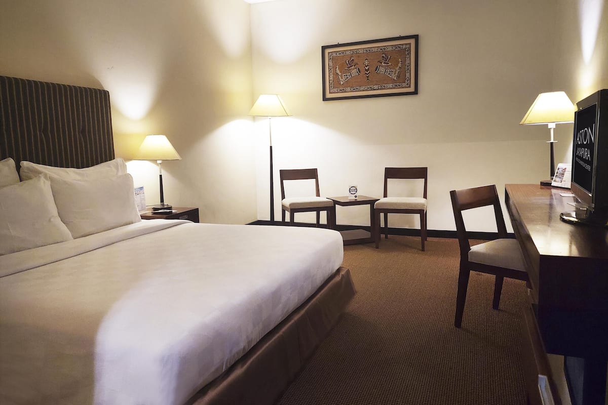 A hotel room with a large bed, two chairs, a small table, a desk with a computer, and two lamps.