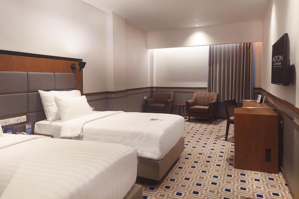A hotel room with two beds, a desk, a chair, and a television.