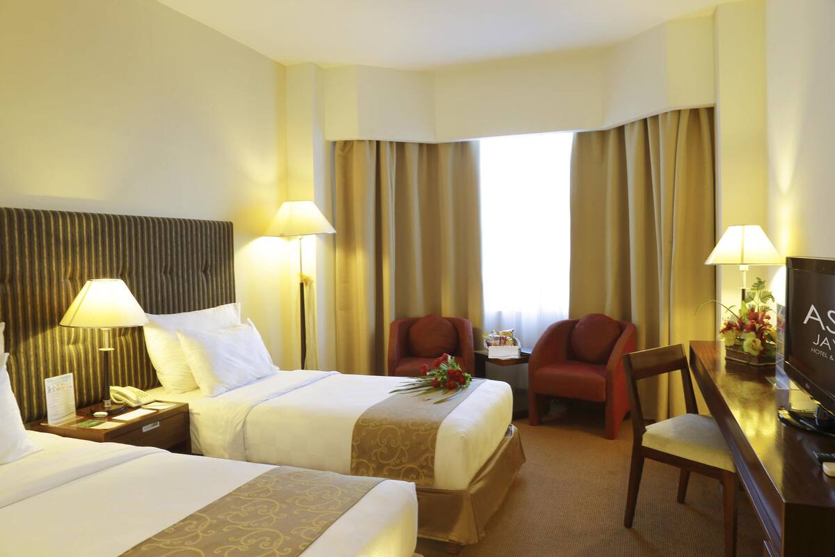 A hotel room with two beds, a desk with a TV, a chair, and a window with curtains.