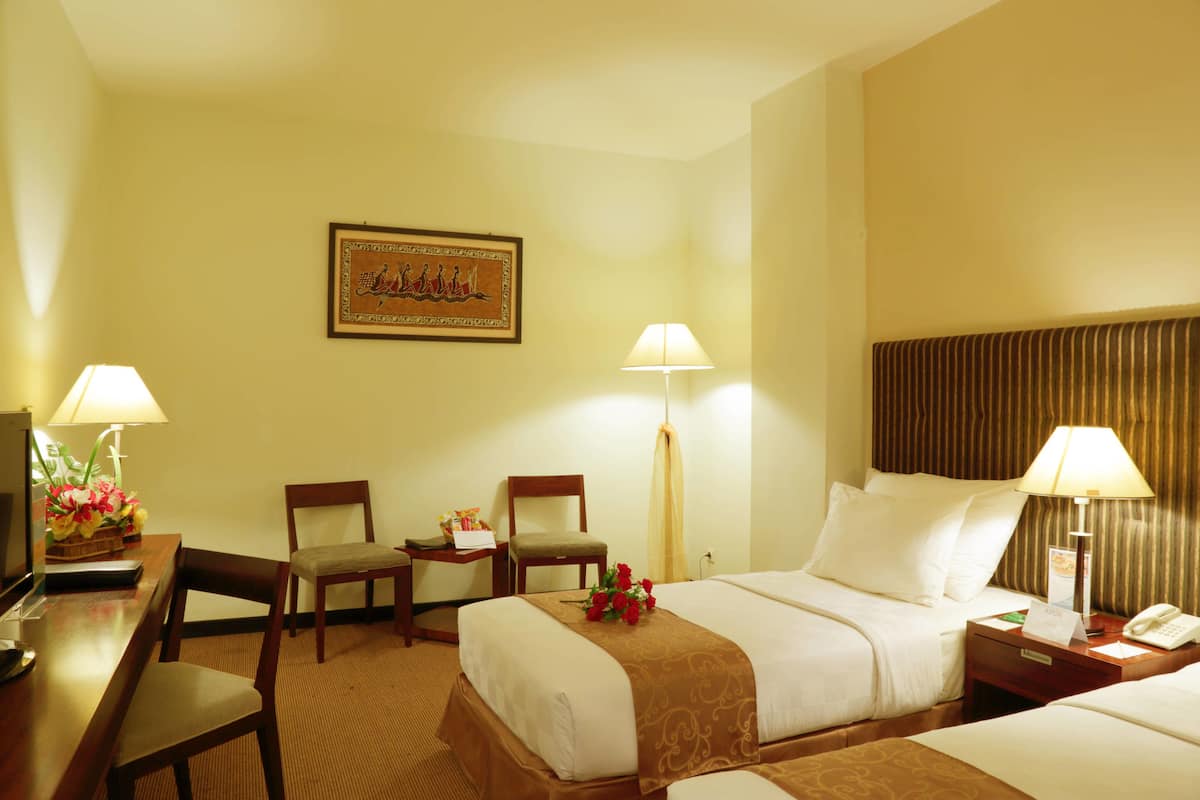 A hotel room with two beds, a desk, chairs, lamps, and a framed picture on the wall.