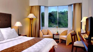 A hotel room with a large bed, two armchairs, a small table with a vase, and a television. - Aston Jayapura Hotel & Convention Center (Jayapura)