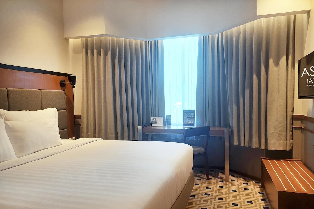 A hotel room with a large bed, a desk, and a TV.