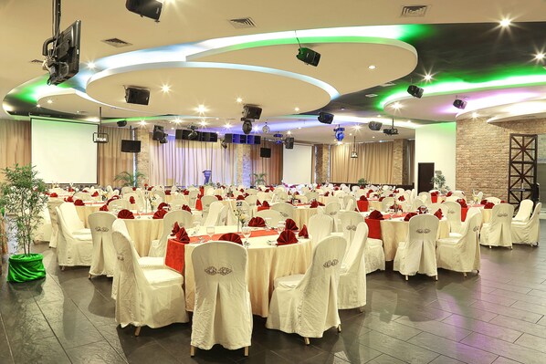 A banquet hall with round tables, white chairs, and a stage.