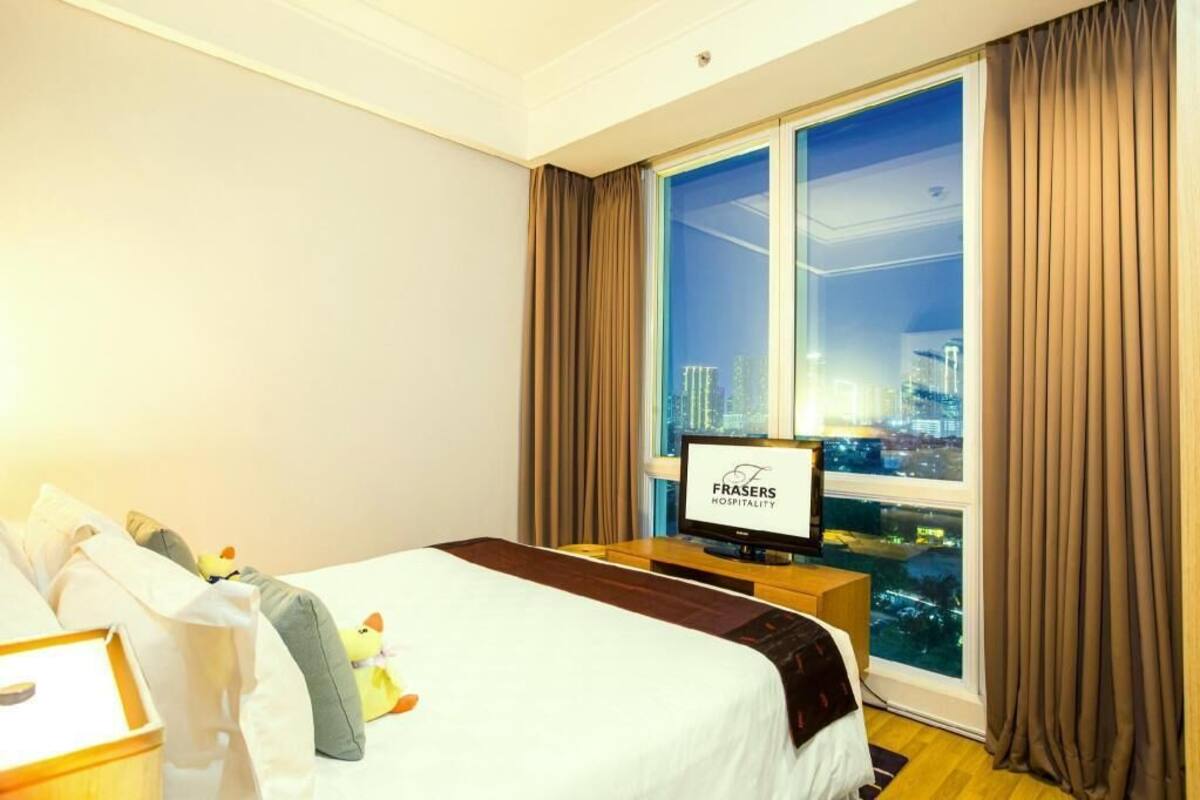 A hotel room with a bed, a television, a window with curtains, and a city view.