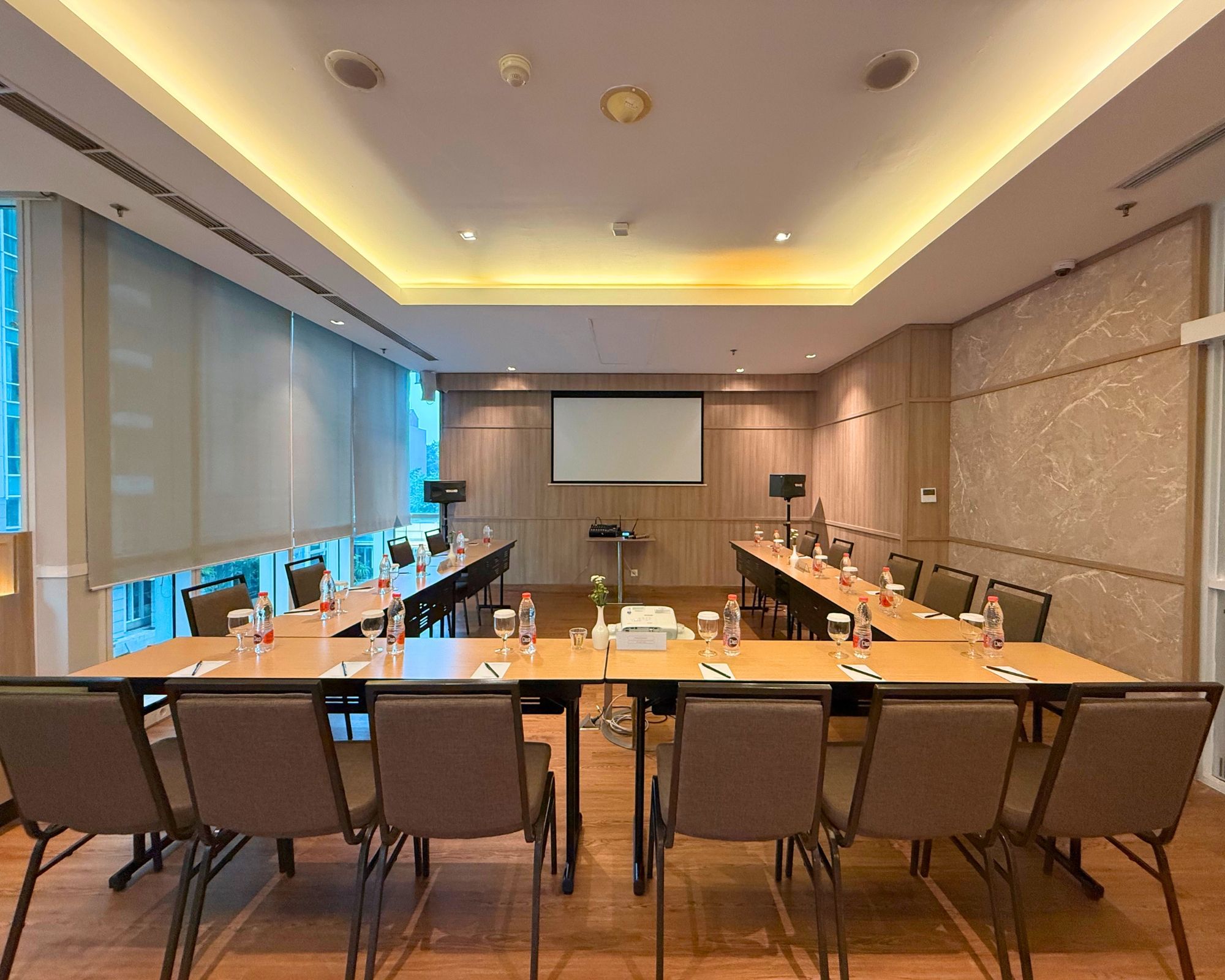 Un salón de conferencias con una larga mesa, sillas y una pantalla de proyector.