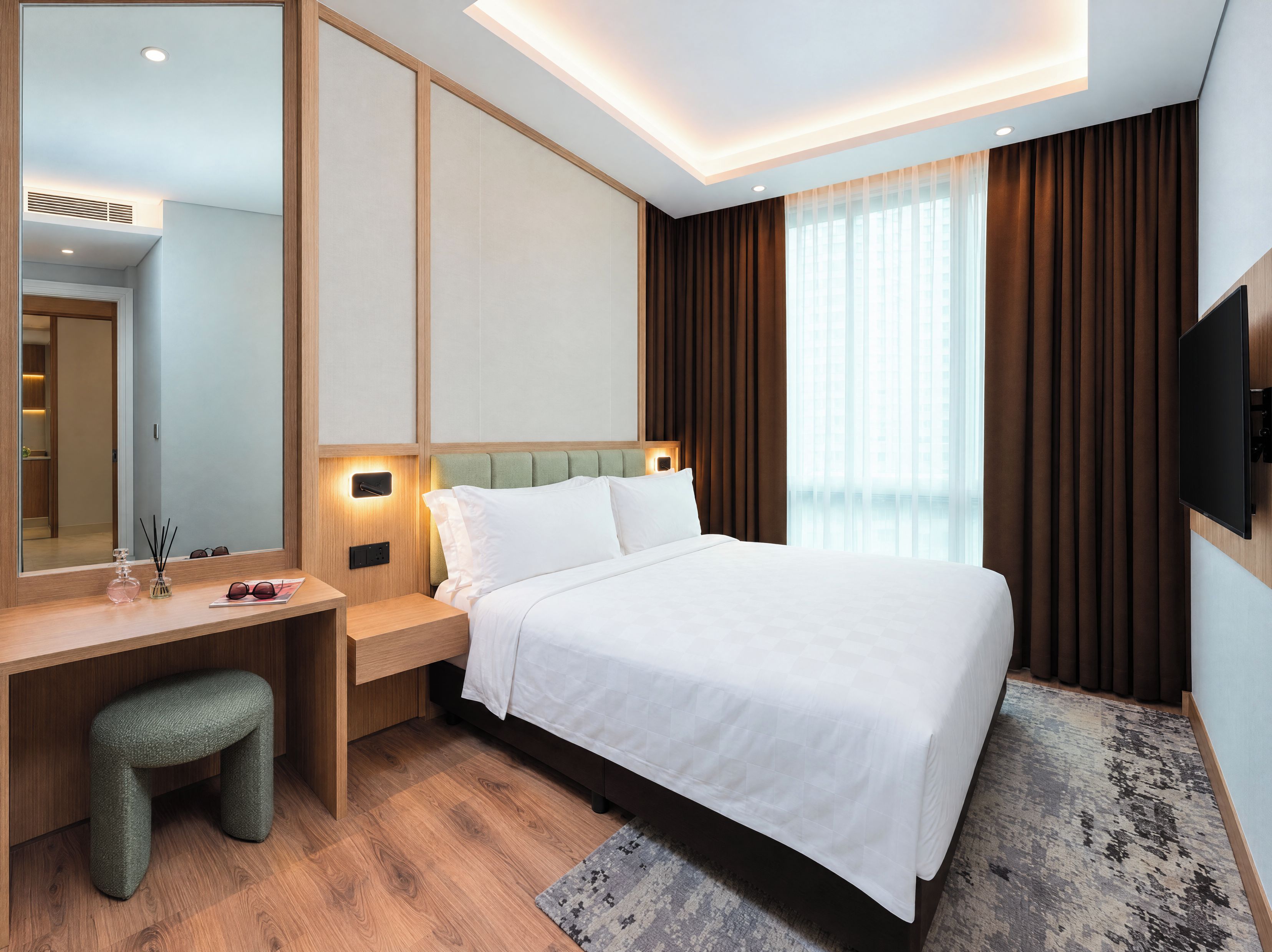 A hotel room with a bed, a desk, a chair, a mirror, and a TV.