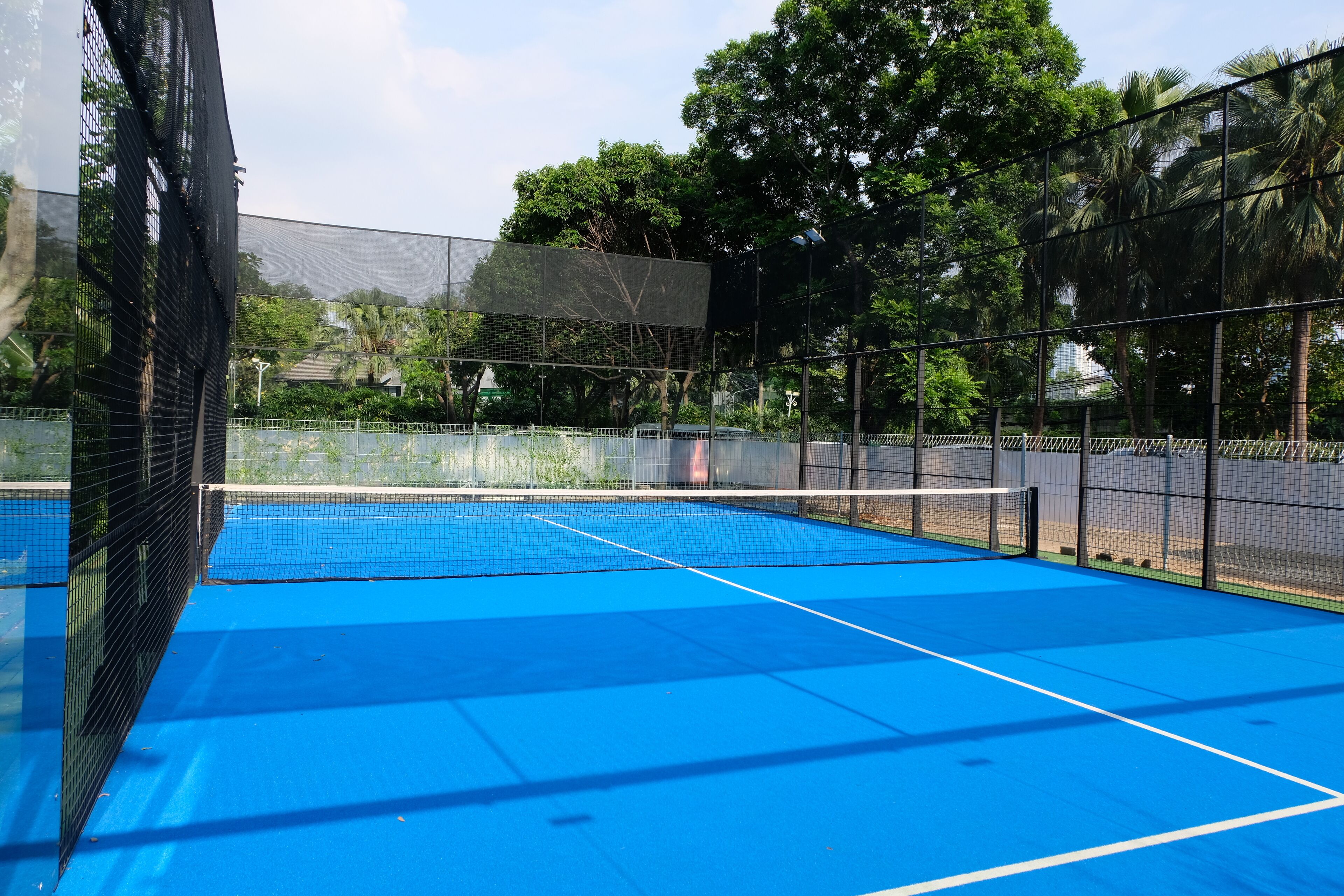 An indoor tennis court with a blue surface, surrounded by a black net and enclosed by a fence.
