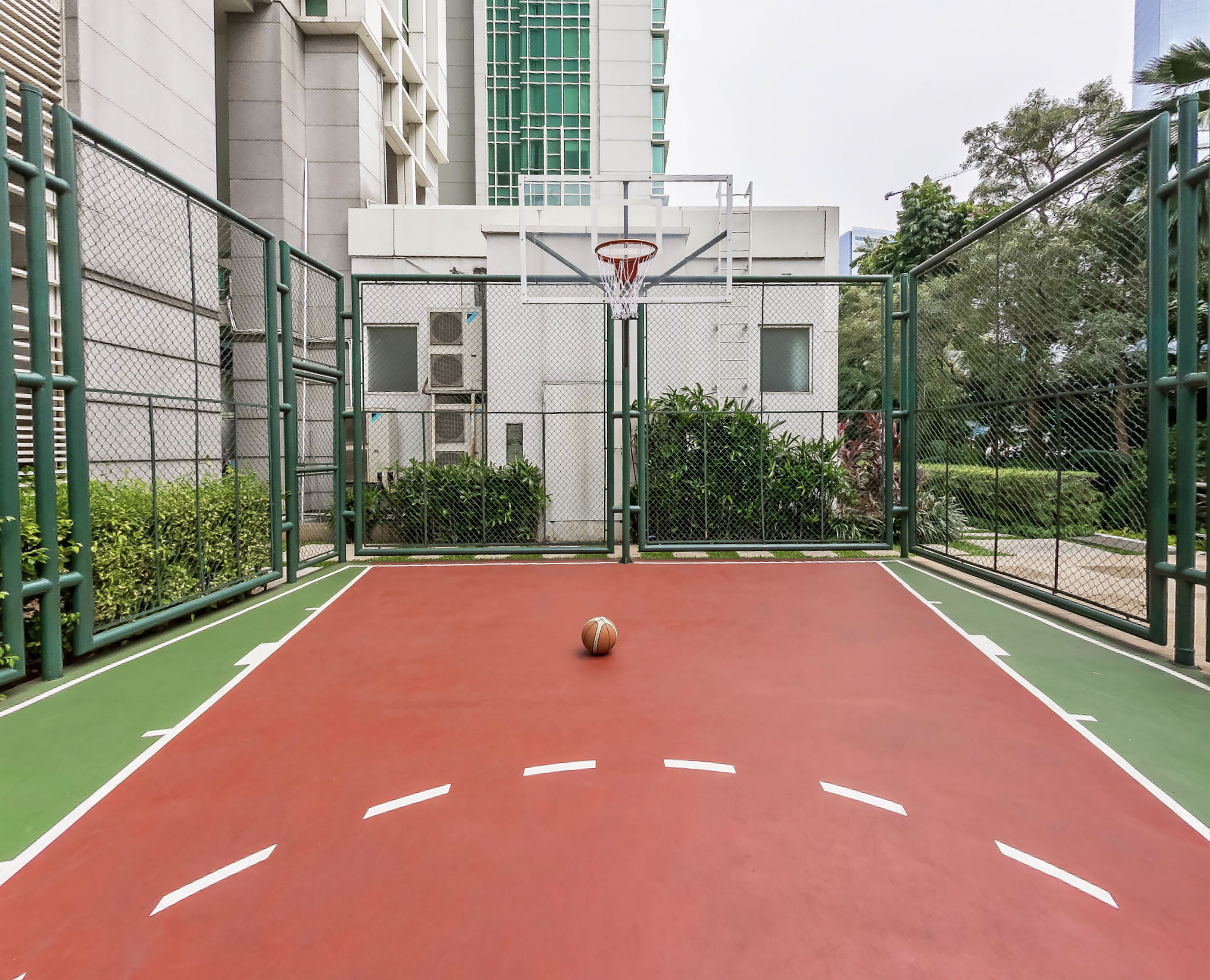 Een buitenbasketbalveld met een net, omringd door een hek van gaas en groen.