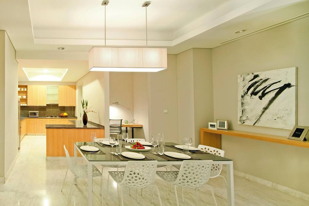 A modern dining area with a glass table, white chairs, and a contemporary pendant light.