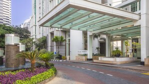 A modern hotel entrance with a covered walkway, palm trees, and a landscaped area with purple flowers.