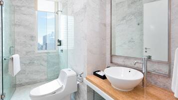 A modern bathroom with a glass-enclosed shower, a white toilet, a large sink with a mirror, and a view of the city through the shower door.
