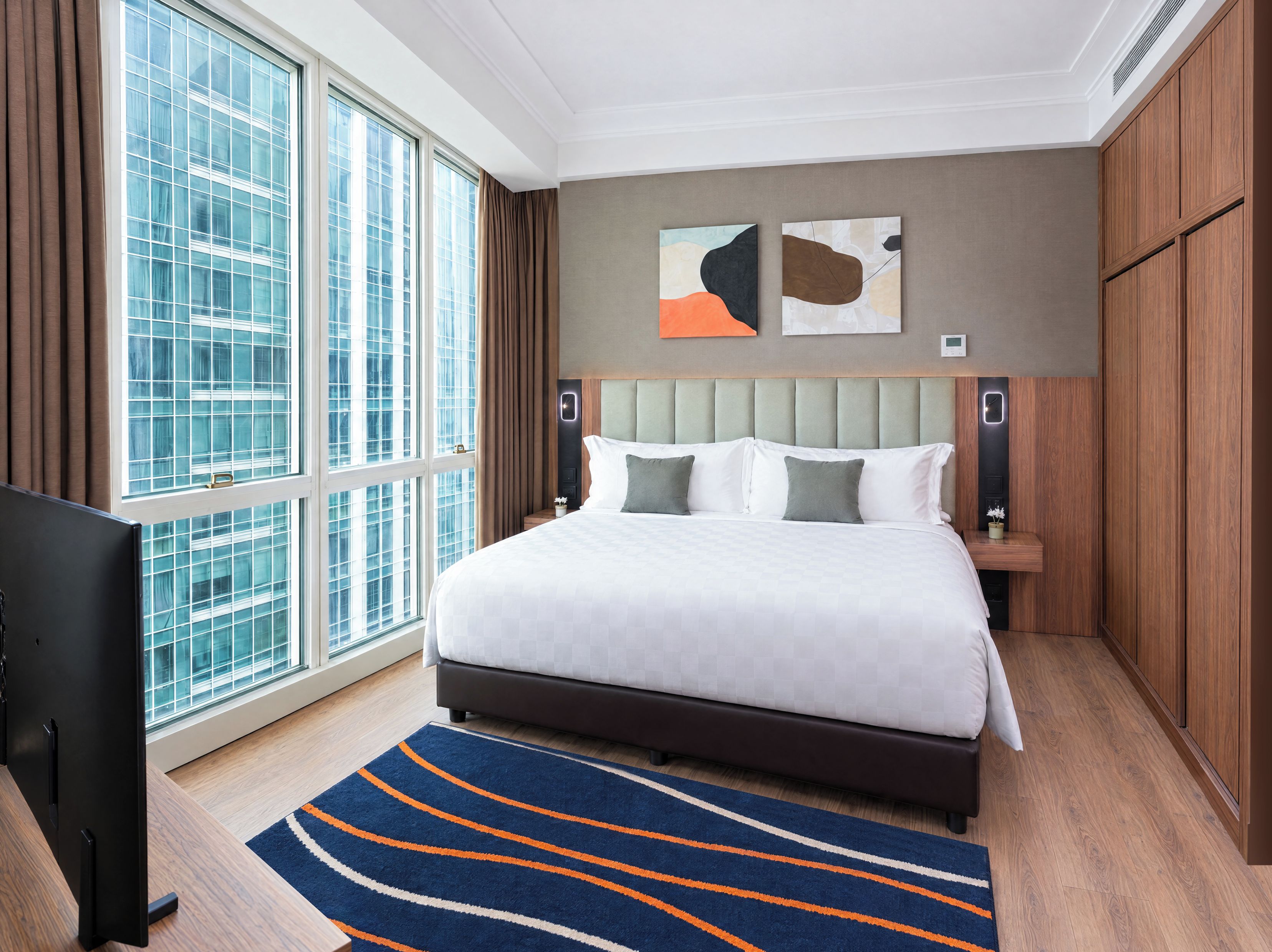A hotel room with a large bed, a TV, a window with curtains, and artwork on the wall.