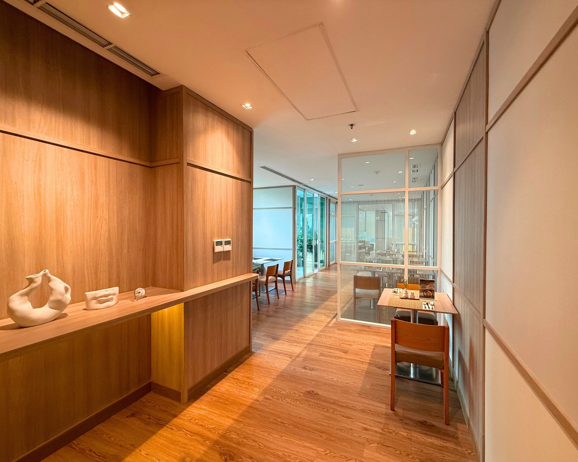 A modern interior with a wooden reception desk, a glass partition, and a dining area with chairs and tables.