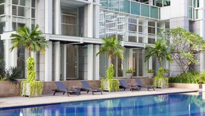 A modern building with a swimming pool, palm trees, and lounge chairs.