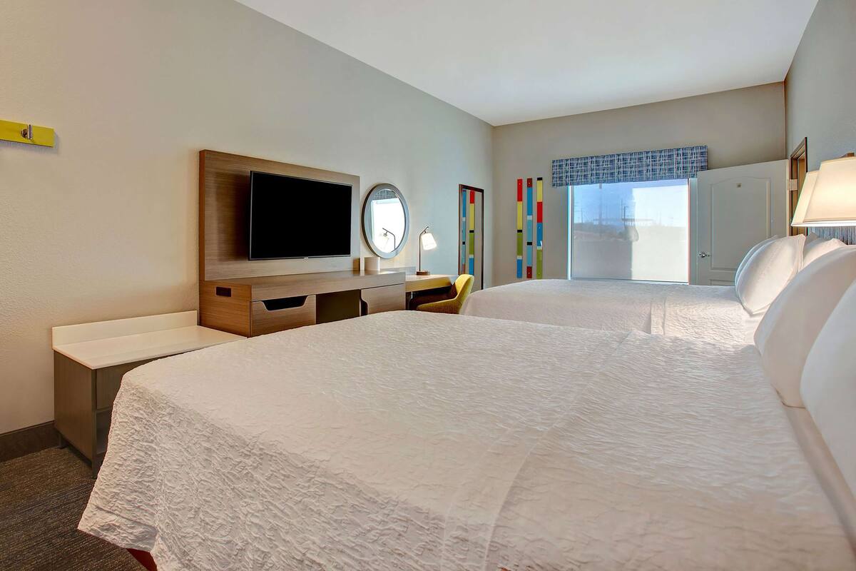 A hotel room with a large bed, a desk with a flat-screen TV, a mirror, and a window with a view.