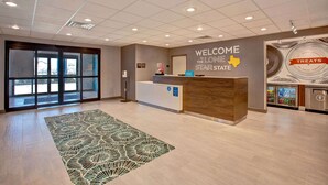 A hotel reception area with a reception desk, a welcome sign, a 'Treats' display, and a patterned rug. - Hampton Inn & Suites Borger (Borger)