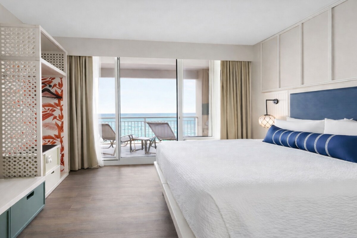 Une chambre d’hôtel comprenant un lit, une télévision, un balcon avec vue sur la mer et un coin salon.