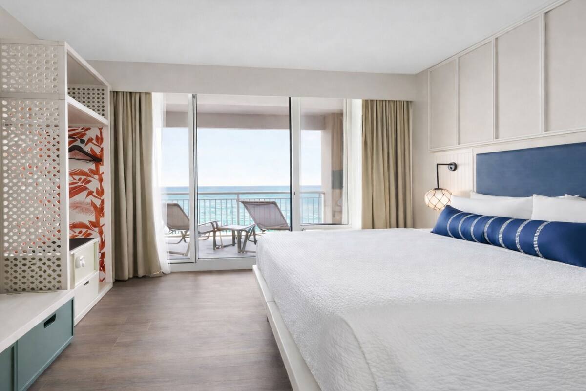 Een hotelkamer met een bed, een televisie, een balkon met uitzicht op zee en een zithoek.