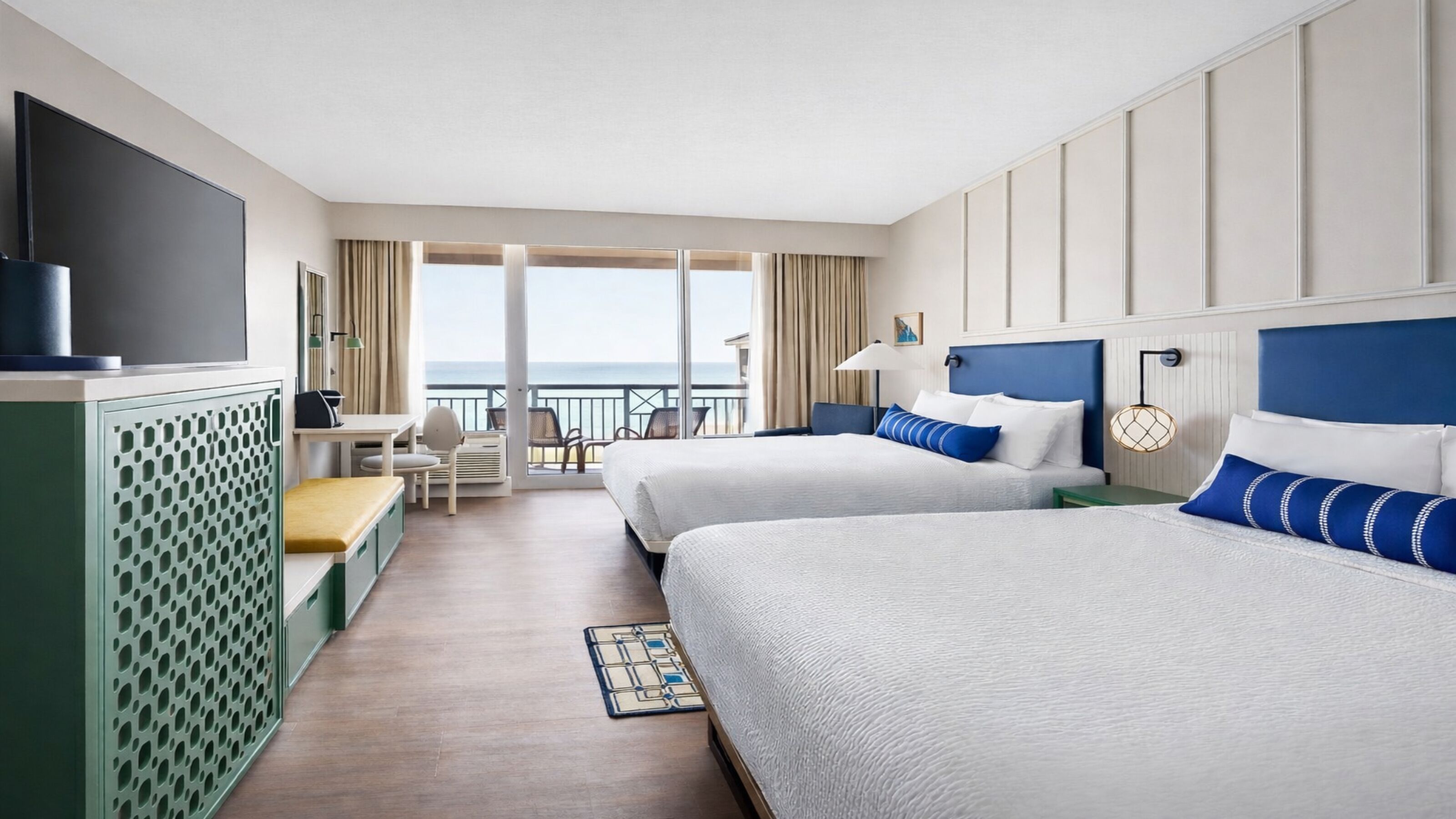 Camera d'albergo con due letti, televisione, scrivania e balcone con vista sull'oceano.