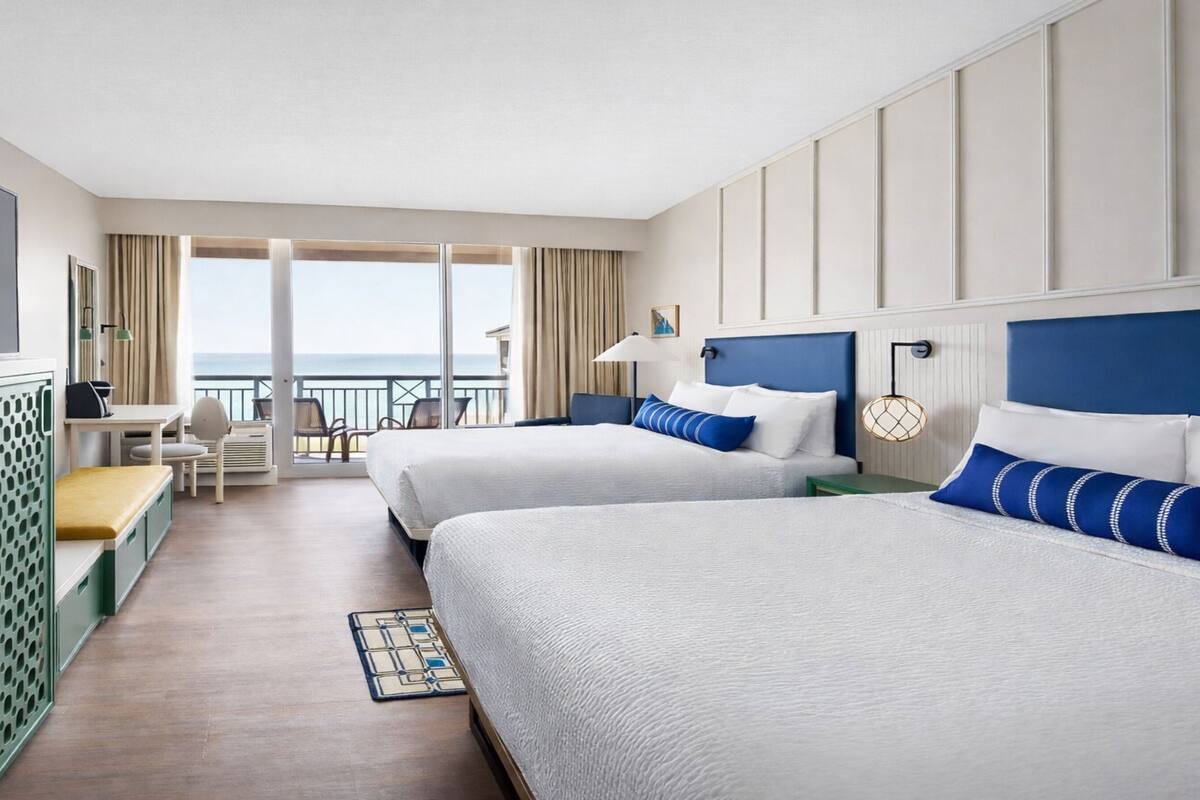 Een hotelkamer met twee bedden, een televisie, een bureau en een balkon met uitzicht op de oceaan.
