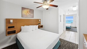 Hotelkamer met een groot bed, een plafondventilator, een schilderij aan de muur en uitzicht op zee door een open deur.