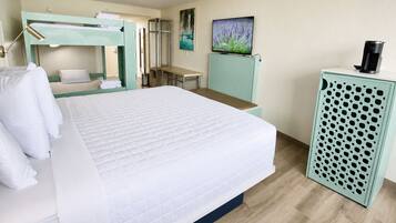 A hotel room with a bed, a desk, a bunk bed, a mirror, a painting, and a coffee machine.
