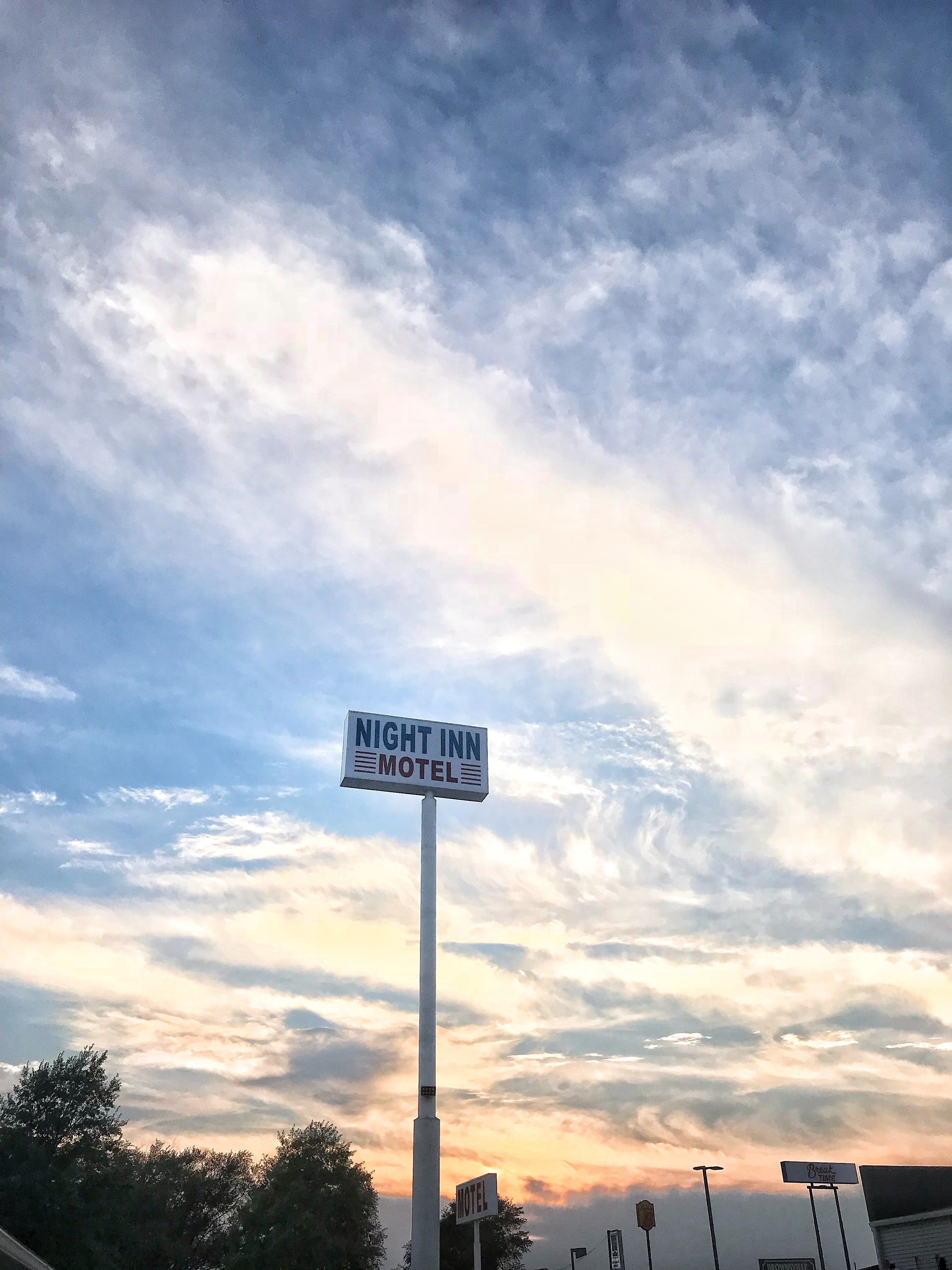 A sign for the Night Inn Motel against a sky with clouds.
